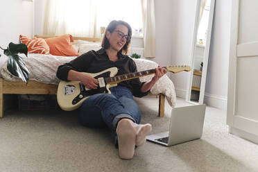 Woman learning guitar watching tutorial on laptop at home - ASGF03574