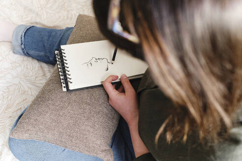 Frau skizziert auf Spiralbuch zu Hause - ASGF03575