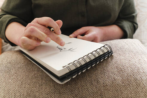 Frau skizziert auf Spiralbuch über Kissen zu Hause - ASGF03576