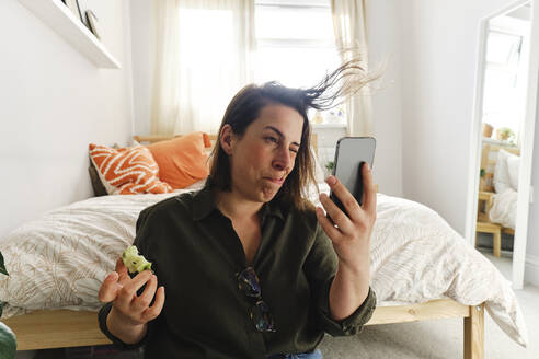 Frau bläst sich die Haare und macht ein Selfie mit ihrem Smartphone zu Hause - ASGF03582
