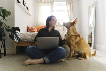 Freelancer with laptop sitting cross-legged by dog at home - ASGF03584