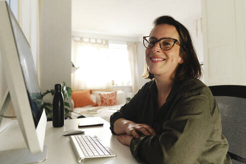 Smiling freelancer with computer at desk in home office - ASGF03589