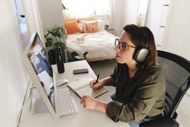 Freiberufler mit kabellosen Kopfhörern bei der Vorbereitung einer Strategie im Home Office - ASGF03592