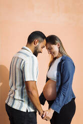 Mann hält Hände und steht mit schwangerer Frau vor einer Mauer - DCRF01580