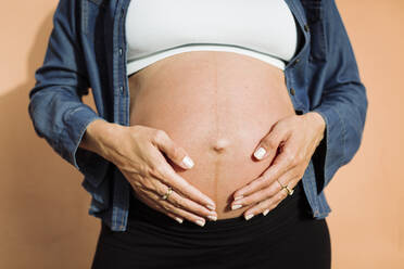 Schwangere Frau mit Händen auf dem Bauch vor einer Wand - DCRF01583