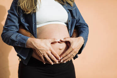 Schwangere Frau macht Herzform auf dem Bauch mit Mann vor der Wand - DCRF01584