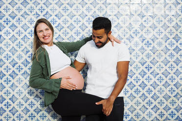 Glücklicher Mann mit schwangerer Frau vor einer gemusterten Kachelwand - DCRF01609
