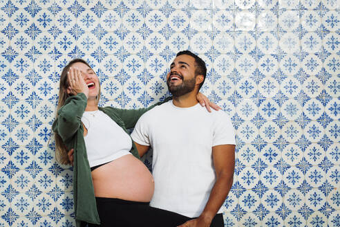 Schwangere Frau hat Spaß mit Mann vor gemusterter Kachelwand - DCRF01610