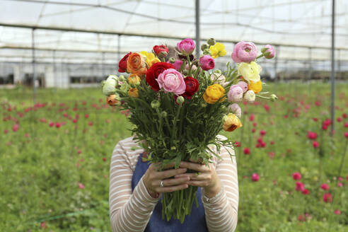 Farmer covering face with fresh bunch of flowers in greenhouse - SYEF00379