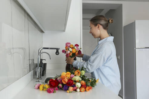 Frau arrangiert Ranunkel in Vase auf Küchentisch zu Hause - SYEF00388