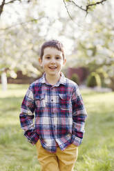 Lächelnder Junge mit Händen in den Taschen im Hinterhof stehend - ONAF00514