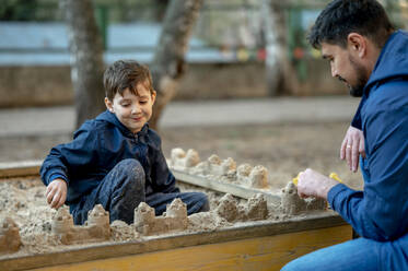 Vater und Sohn bauen Sandburgen im Sandkasten im Park - ANAF01382
