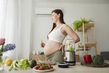 Schwangere Frau mit Hand auf der Hüfte in der Küche zu Hause stehend - ALKF00277