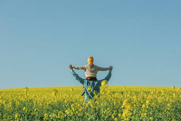 Father carrying son on shoulder in rapeseed field - VSNF00771