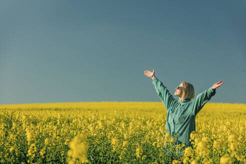 Woman with arms outstretched standing amidst flowers in rapeseed field - VSNF00778