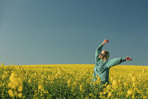 Carefree woman with arms raised standing in rapeseed field - VSNF00779