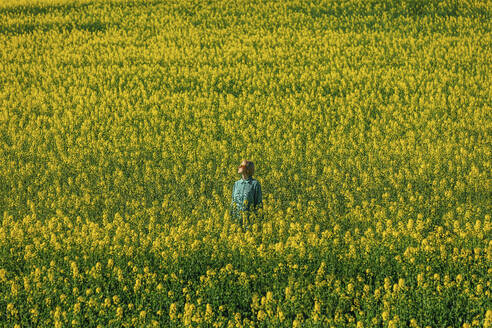 Frau steht inmitten gelber Rapsblüten auf einem Feld - VSNF00781