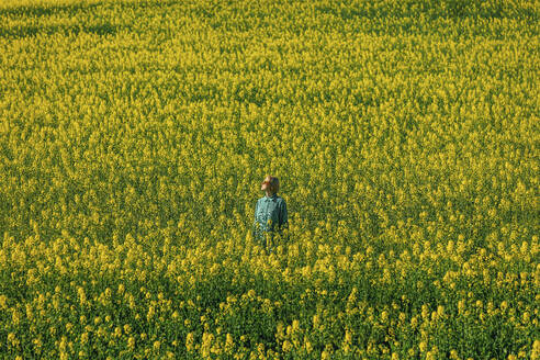 Woman standing amidst yellow rapeseed flowers in field - VSNF00781
