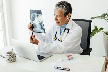 Doctor providing diagnostic care remotely, showing a patient’s x-ray results over a video call. Experienced female radiologist advising her patient in a telehealth visit, providing top notch medical care from her office. - JLPSF29550