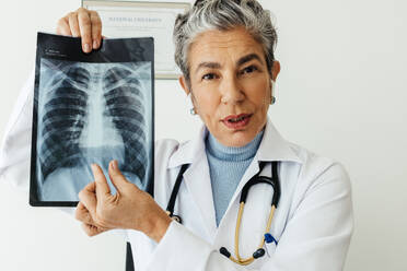 Eine Radiologin erläutert die Ergebnisse einer Lungenuntersuchung im Rahmen einer telemedizinischen Konsultation. Ein älterer Arzt zeigt einem Patienten das Röntgenbild während einer virtuellen Konsultation. Eine erfahrene Ärztin führt eine Videokonferenz in ihrer Praxis durch. - JLPSF29554