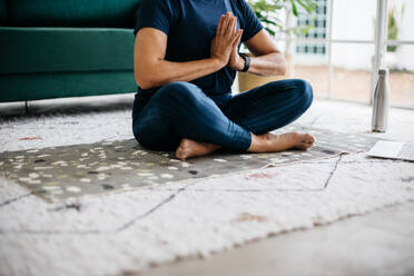 Frau meditiert in Gebetshaltung zu Hause, in Fitnesskleidung auf dem Boden sitzend. Ältere Frau, die einen Online-Yogakurs besucht und gesunde Atemübungen für inneren Frieden und Gelassenheit praktiziert. - JLPSF29576