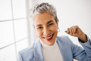 Porträt einer älteren Frau mit grauen Haaren im Geschäftsanzug bei der Arbeit. Erfahrene Geschäftsfrau, die in ihrem Büro lächelt, selbstbewusst und überzeugt von ihren Fähigkeiten als Spitzenkraft. - JLPSF29603