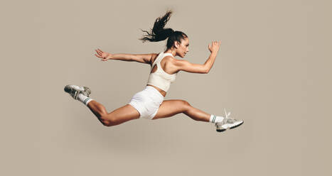 Aktive Sportlerin, die mitten in der Luft läuft und in einem Studio kräftig trainiert. Sportliche Frau, die Kraft- und Ausdauerübungen für bessere Fitness und Leistung kombiniert. Frau, die in Sportkleidung trainiert. - JLPSF29627