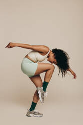 Woman dressed in sportswear gracefully executing an athletic pose in a studio, showing her flexibility and balance. With her expressive body movement, she exhibits the confidence that comes with being physically fit. - JLPSF29668