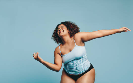 Plus size woman dancing with flexibility and agility in a studio, displaying her confidence in her own body. Woman in sportswear expressing body positivity and embracing her fitness journey. - JLPSF29675