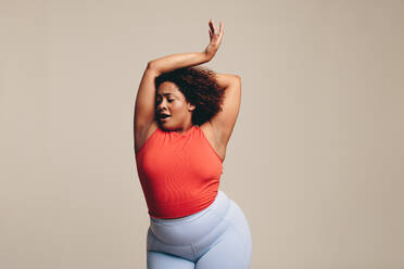 Eine fitte, kurvige Frau, die in einem Studio ein Tanz-Workout genießt, eine ausdrucksstarke Form der körperlichen Betätigung. Eine Frau, die ihren Körper feiert, sich selbstbewusst bewegt und sich durch Tanz ausdrückt. - JLPSF29684