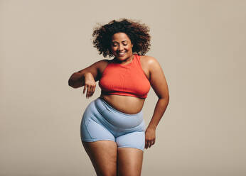 Cheerful large african woman with a medicine ball on brown background. Plus  size female in sports clothing looking at camera and laughing. stock photo