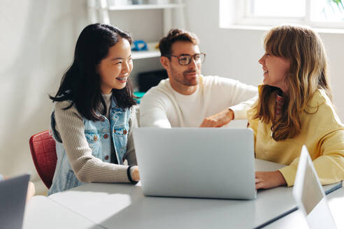 Tutor helping young female students with a computer science lesson in a classroom. Two young girls smiling and engaging with their teacher as they learn coding and digital education with a laptop. - JLPSF29722