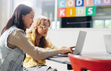 Zwei Kinder arbeiten in einem Computerakademie-Klassenzimmer zusammen, um Programmieren zu lernen. Junge weibliche Klassenkameradinnen engagieren sich und unterstützen sich gegenseitig, um Informatik und Technologie zu beherrschen. - JLPSF29728