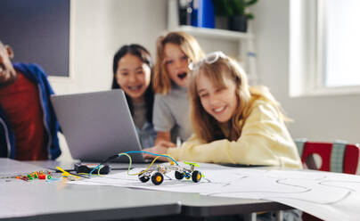 Practical robot programming lesson for children using a laptop to control their creations. Primary school kids learning the basics of coding as they program and operate their robotic vehicles. - JLPSF29733