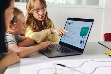Ein intelligentes Mädchen erklärt seinen Mitschülern im Informatikunterricht das Programmieren von Robotern. Jungen und Mädchen helfen sich gegenseitig, mithilfe von Lernsoftware Fähigkeiten in der Robotertechnik zu entwickeln. - JLPSF29735