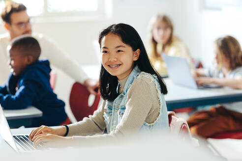 With a smile on her face, a young girl learns to code in a computer-based learning environment, mastering digital literacy and gaining valuable skills in programming and computer science. - JLPSF29752