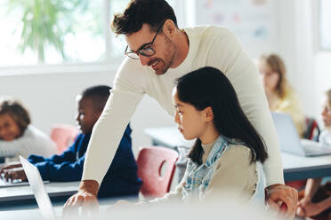 Grundschullehrerin, die einer Schülerin im Rahmen eines Unterrichts zur digitalen Kompetenz beim Programmieren hilft. Ein junges Mädchen lernt unter Anleitung ihrer Lehrerin in einem Klassenzimmer technische Grundkenntnisse. - JLPSF29753