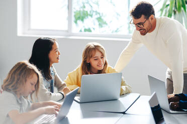 Informatiklehrer, der eine Gruppe junger Schüler in einem Programmierkurs anleitet. Lehrer, der mit den Kindern lernt, auf ihren Laptops zu programmieren, um ihnen eine solide Grundlage für das Programmieren zu vermitteln. - JLPSF29755