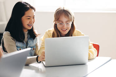 Fröhliche Schülerinnen, die sich gegenseitig bei einer Aufgabe zur digitalen Kompetenz in einem Klassenzimmer unterstützen. Zwei Kinder, die sich in einer Umgebung, die sich auf computergestütztes Lernen konzentriert, miteinander beschäftigen. - JLPSF29757