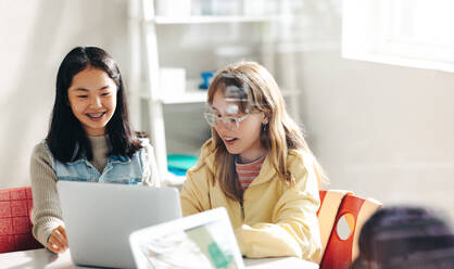 Zwei Schülerinnen, die sich im Informatikunterricht zusammentun und einen Laptop benutzen, um ihre Aufgabe zu erfüllen. Glückliche Kinder, die eine Schule in einem modernen Umfeld besuchen, das computergestütztes Lernen nutzt. - JLPSF29759