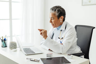 Ältere Ärztin, die in ihrer Praxis eine virtuelle Konsultation durchführt und über einen Videoanruf mit einem Patienten spricht. Erfahrene Mediziner, die medizinische Versorgung mit Hilfe von Technologie anbieten, eine Praxis, die als Telemedizin bekannt ist. - JLPSF29777