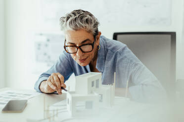 Eine erfahrene Architektin analysiert in ihrem Büro ein architektonisches Gebäudemodell. Ein erfahrener Ingenieur nutzt die 3D-Modellierung, um einen Hausentwurf zu erneuern und zu verbessern. - JLPSF29815