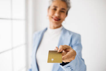 Ältere Geschäftsfrau, die in ihrem Büro eine elektronische Zahlung mit einer goldenen Kreditkarte vornimmt. Reife weibliche Führungskraft, die ein exklusives goldenes Bankkonto nutzt, um professionelle Zahlungen und bargeldlose Geschäftstransaktionen durchzuführen. - JLPSF29847
