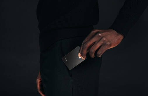 Schwarzer Geschäftsmann, der eine Premium-Kreditkarte aus der Tasche zieht, um eine bargeldlose Zahlung vorzunehmen. Professioneller Mann in schwarzer Kleidung, der die Vorteile seines exklusiven Bankkontos nutzt. - JLPPF01649