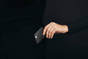 Electronic Banking wird demonstriert, als eine weibliche Hand in einem Studio eine schwarze Kreditkarte aus der Tasche eines Mannes zieht. Eine Frau hält eine Premium-Bankkarte in der Hand, die kontaktloses Bezahlen per Tap and Pay ermöglicht. - JLPPF01652