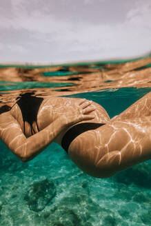Unterwasser-Seitenansicht von abgeschnittenen anonymen schwangere Frau im Bikini Schwimmen in transparenten blauen Meerwasser mit Riffen und Fischen im Urlaub - ADSF43770