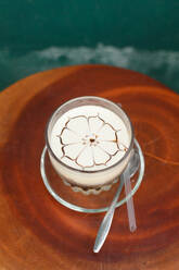 Transparentes Glas Tasse mit aromatischen vietnamesischen Cappuccino mit Kunst auf Schaum auf runde Platte mit Löffel platziert - ADSF43863