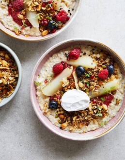 Draufsicht auf leckere, appetitliche Haferflocken mit Blaubeeren und Himbeeren mit Granola und Äpfeln in einer Schüssel mit Sahne serviert - ADSF43901