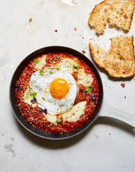 Draufsicht auf eine Bratpfanne mit appetitlichem Shakshuka mit Ei und Käse neben Brot auf dem Tisch - ADSF43902