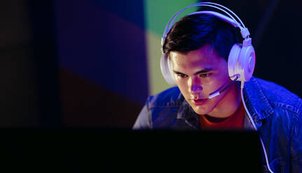 Junger Mann, der müde auf den Bildschirm seines Computerspiels blickt und über den nächsten Zug seines Avatars im virtuellen Videospiel nachdenkt. Männlicher Gamer, der auf einer Online-Streaming-Plattform mit einem Headset spielt. - JLPSF29866